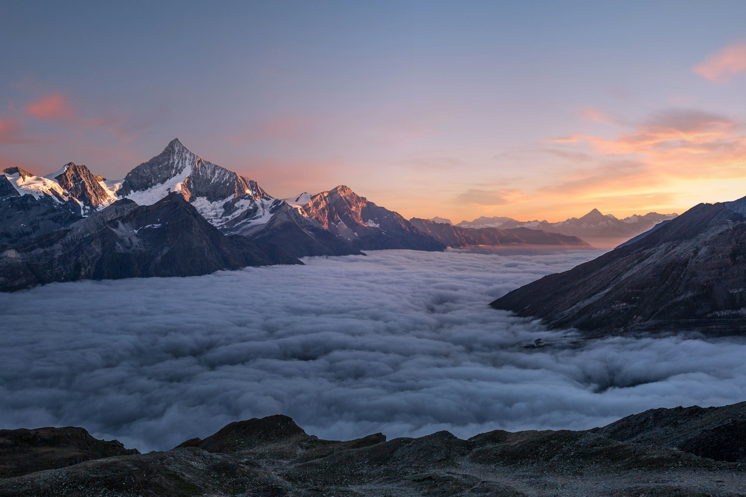 Snow-capped alpine peaks rising above a sea of clouds at sunrise