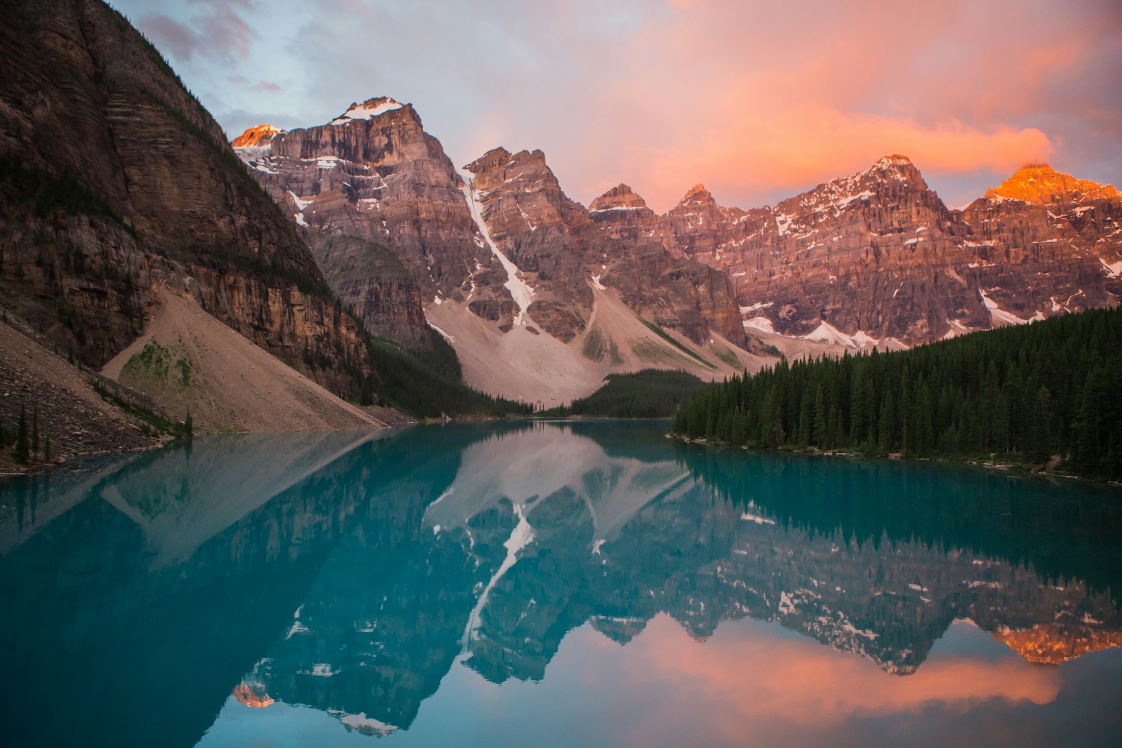 Turquoise mountain lake reflecting a glowing sunset behind rugged peaks