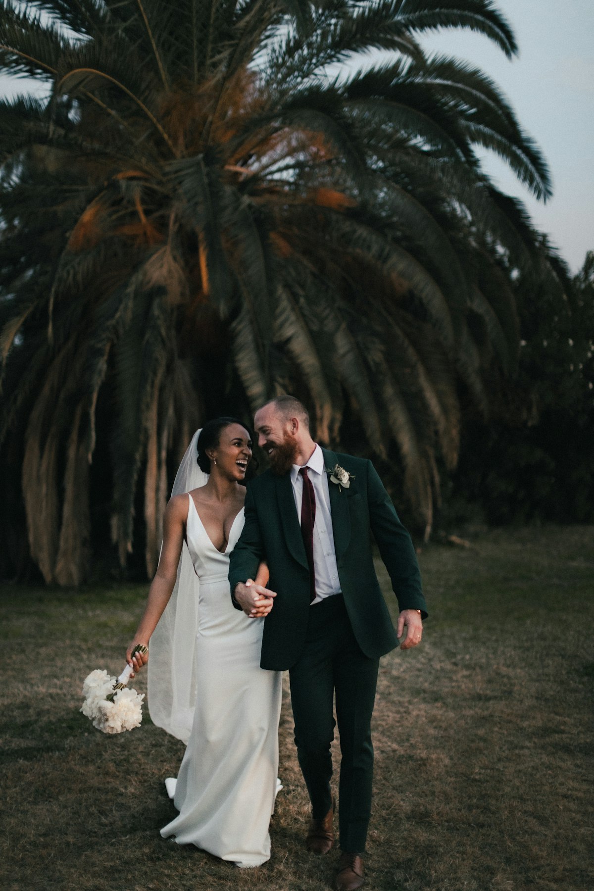 Bride and groom walking together beneath palm trees