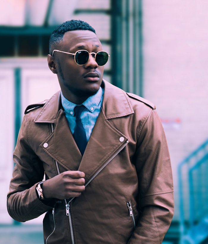 Man in a tan leather jacket and round sunglasses
