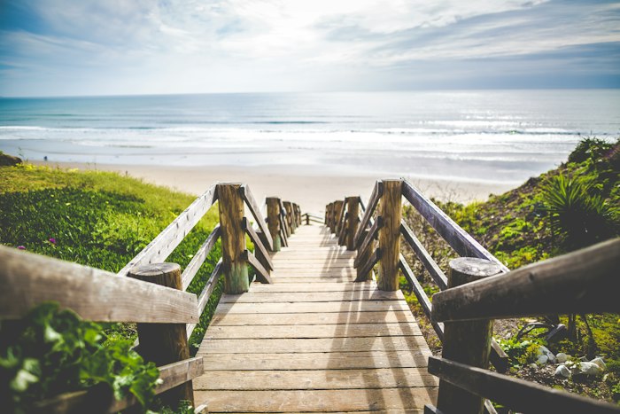 Wooden boardwalk stairs descending to a sunlit beach